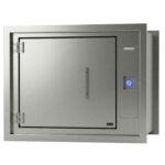 Durchreiche von MNT Kwint International in der Wandeinbau-Ausführung – 3/4-Ansicht mit geschlossener Türe, zwei Edelstahlscharnieren, mittigem Griff, blauem LED-Druckknopf, UNLOCKED/LOCKED-Statusanzeige und 15 mm Pb Bleiabschirmung. Gehäuse gebürsteter Edelstahl AISI 304.